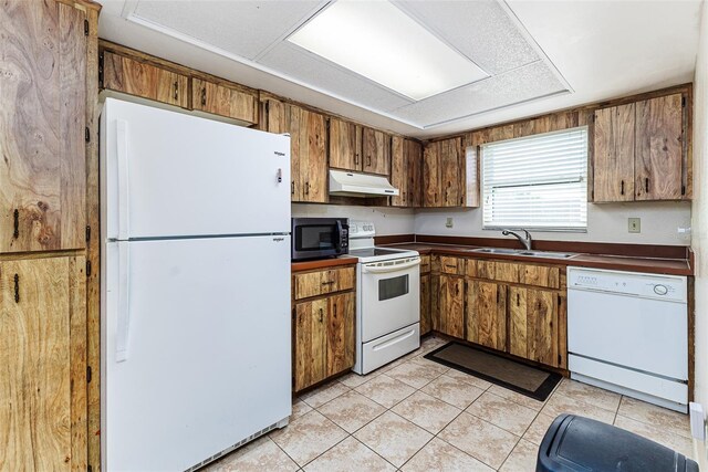 kitchen featuring dark countertops, brown cabinets, a sink, under cabinet range hood, and white appliances