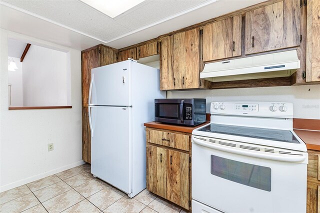 kitchen with light tile patterned floors, brown cabinetry, under cabinet range hood, and white appliances