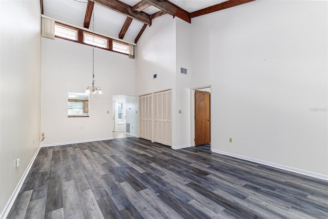 unfurnished living room with a notable chandelier, beam ceiling, high vaulted ceiling, dark wood finished floors, and a wealth of natural light
