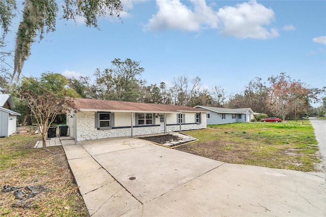 single story home with covered porch, driveway, stone siding, and a front yard