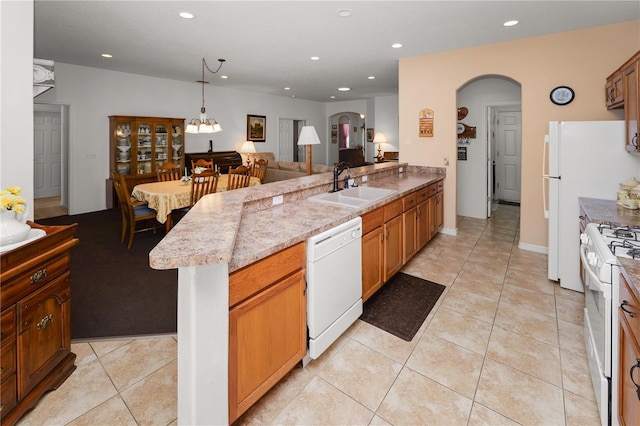 kitchen with arched walkways, white appliances, a sink, open floor plan, and pendant lighting