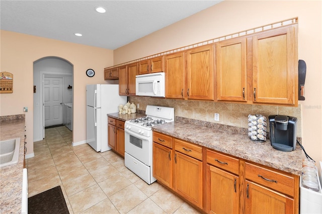 kitchen with white appliances, arched walkways, light stone countertops, backsplash, and light tile patterned flooring