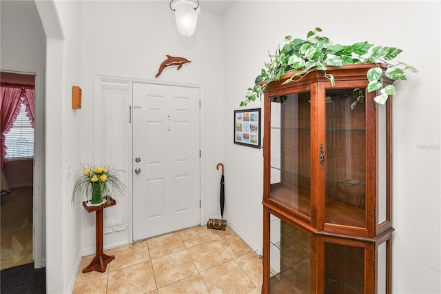 foyer featuring arched walkways, light tile patterned flooring, and baseboards