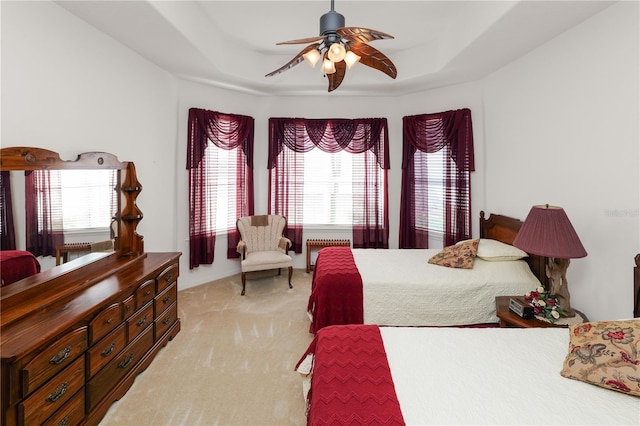 bedroom with a tray ceiling, a ceiling fan, and light colored carpet