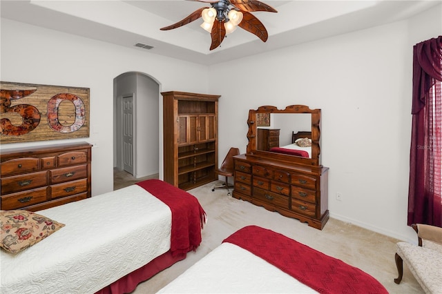 bedroom featuring arched walkways, ceiling fan, light colored carpet, visible vents, and a tray ceiling