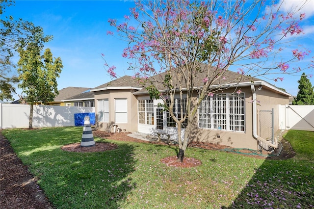 rear view of house with a yard, a fenced backyard, a gate, and stucco siding