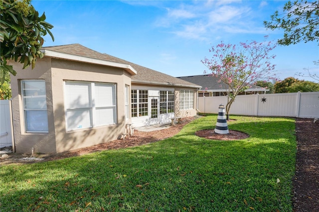 rear view of house featuring a shingled roof, fence, a lawn, and stucco siding