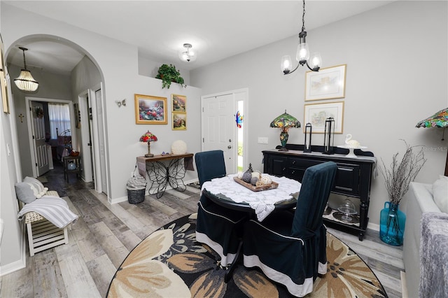 dining space featuring arched walkways, a notable chandelier, baseboards, and wood finished floors