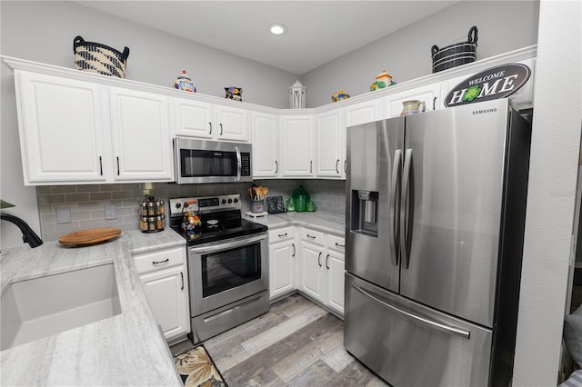 kitchen with a sink, white cabinetry, appliances with stainless steel finishes, light wood-type flooring, and light stone countertops