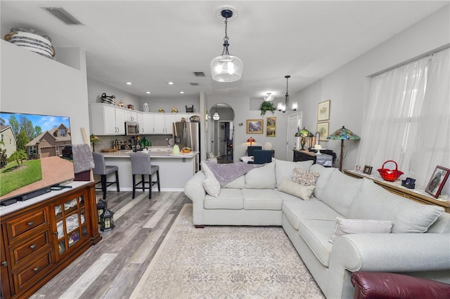 living room featuring light wood-style flooring, visible vents, arched walkways, and recessed lighting