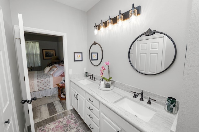 ensuite bathroom featuring connected bathroom, double vanity, a sink, and wood finished floors