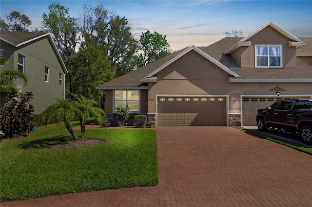 view of front facade with decorative driveway, stone siding, a yard, and stucco siding