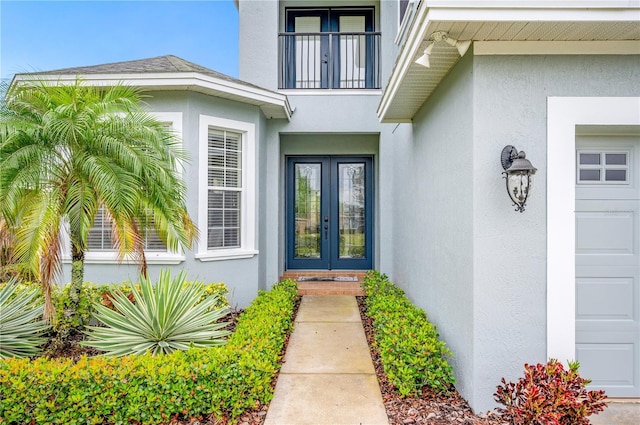 doorway to property with a garage, french doors, a balcony, and stucco siding