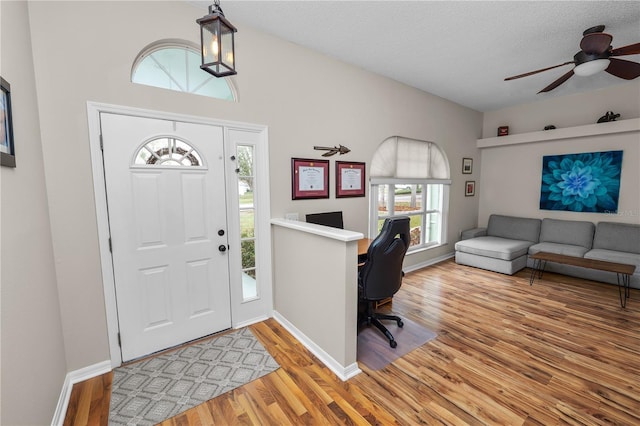 foyer entrance featuring baseboards, vaulted ceiling, light wood-style flooring, and a textured ceiling