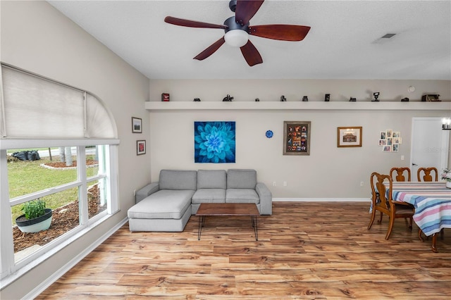 living area featuring baseboards, light wood-style flooring, visible vents, and a ceiling fan