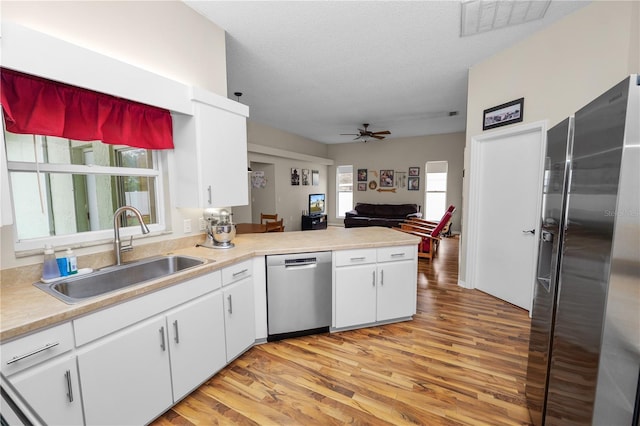 kitchen featuring stainless steel appliances, a peninsula, a sink, white cabinets, and light countertops