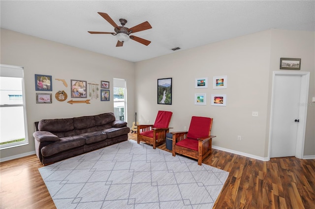 living area featuring a ceiling fan, light wood-type flooring, visible vents, and baseboards