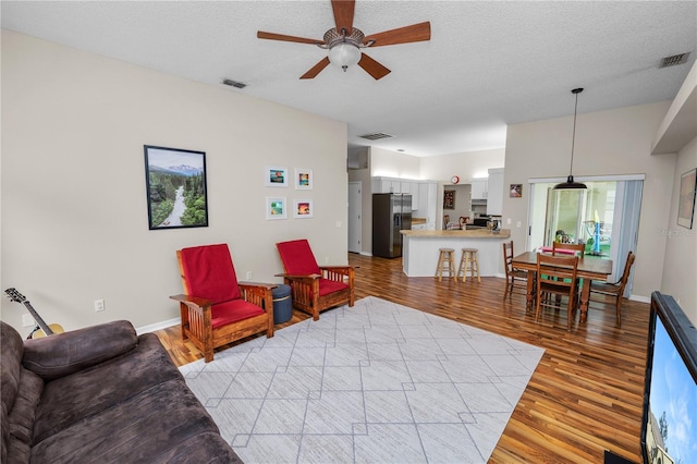 living room with a textured ceiling, light wood finished floors, and visible vents