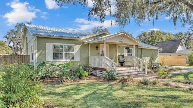 view of front facade with metal roof, covered porch, fence, a front lawn, and stucco siding