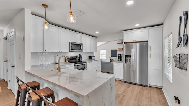 kitchen featuring light stone counters, a peninsula, white cabinetry, appliances with stainless steel finishes, and decorative light fixtures