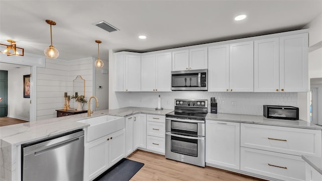 kitchen featuring decorative light fixtures, visible vents, appliances with stainless steel finishes, white cabinets, and a sink