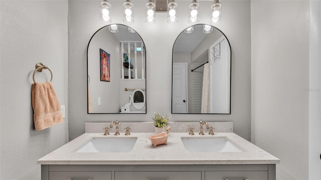 full bathroom with double vanity, walk in shower, a sink, and a textured wall