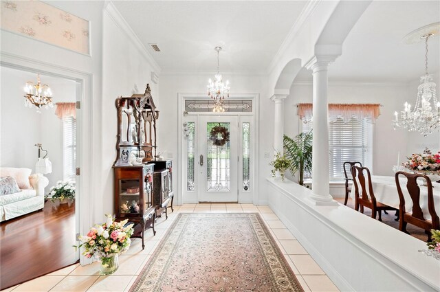 tiled entrance foyer featuring ornate columns, visible vents, a wealth of natural light, and a notable chandelier