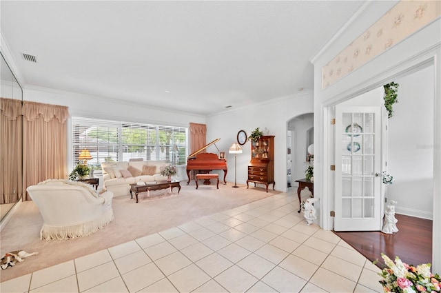 living area featuring light tile patterned floors, visible vents, arched walkways, light colored carpet, and ornamental molding