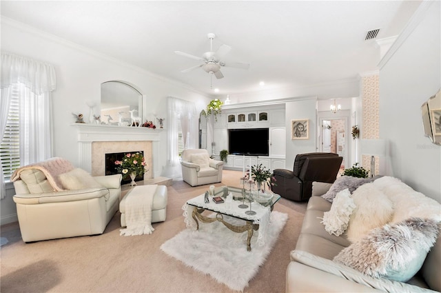 living area featuring ceiling fan with notable chandelier, a premium fireplace, visible vents, ornamental molding, and carpet