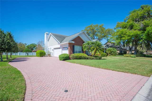 view of front of home with decorative driveway, brick siding, an attached garage, fence, and a front lawn