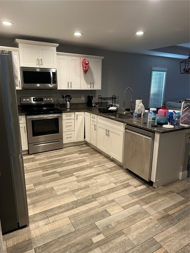 kitchen featuring white cabinets, appliances with stainless steel finishes, a peninsula, a sink, and recessed lighting