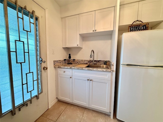 kitchen featuring light tile patterned floors, freestanding refrigerator, white cabinetry, a sink, and light stone countertops