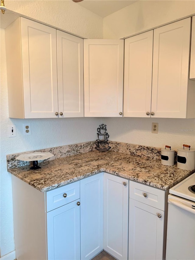 kitchen with light stone counters, white electric range, white cabinetry, and a textured wall