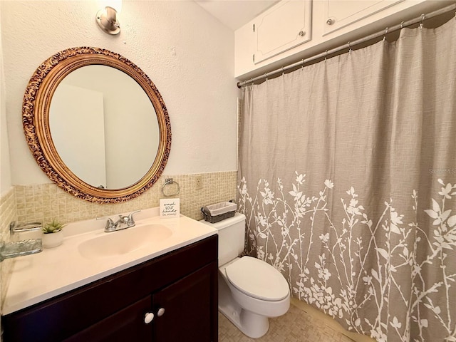 bathroom featuring tile walls, wainscoting, vanity, and toilet