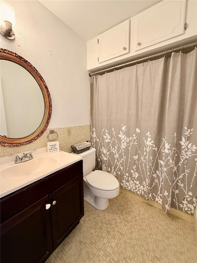 full bath featuring tile walls, a wainscoted wall, vanity, and toilet