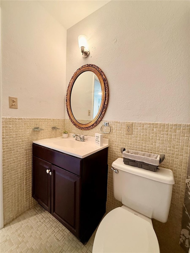 half bathroom with toilet, a wainscoted wall, tile walls, and vanity