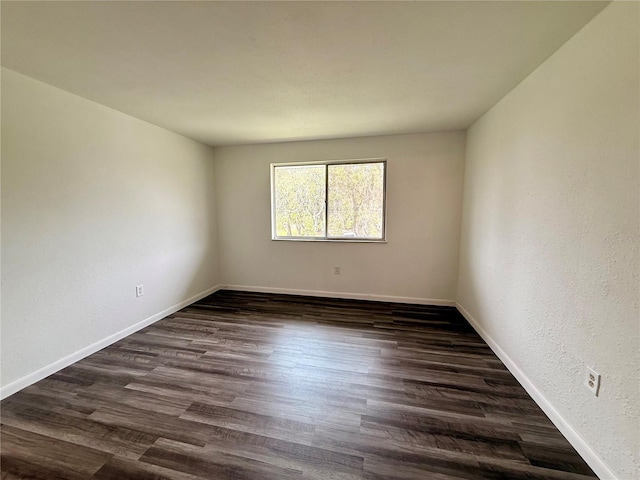 unfurnished room featuring a textured wall, dark wood-style flooring, and baseboards