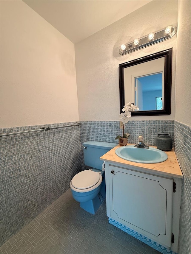 bathroom featuring a wainscoted wall, toilet, vanity, and tile walls