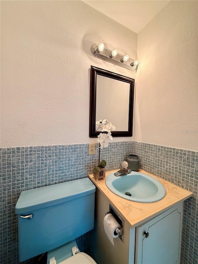 half bathroom with toilet, a wainscoted wall, tile walls, and vanity