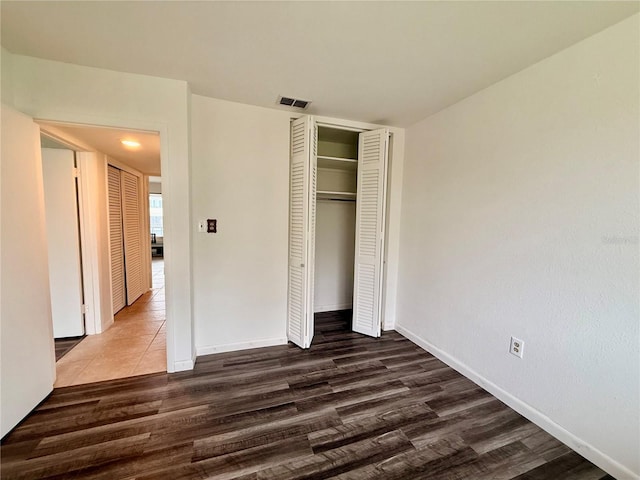 unfurnished bedroom with visible vents, a closet, baseboards, and dark wood-type flooring