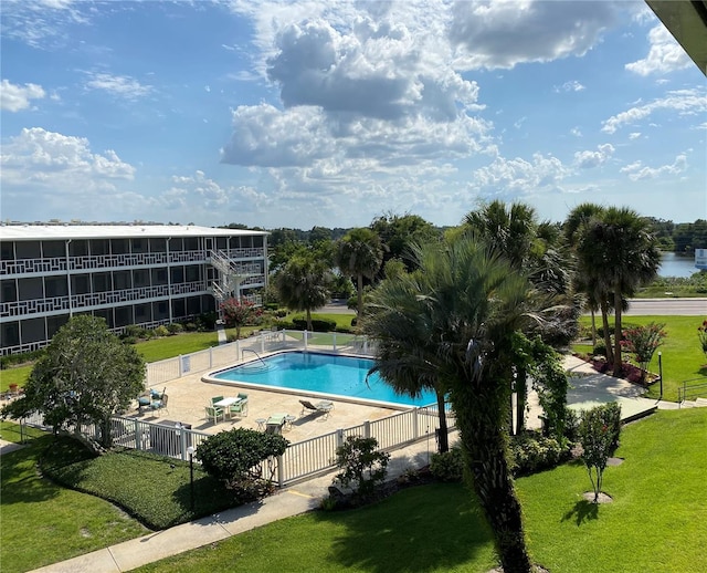 community pool featuring a water view, fence, a lawn, and a patio