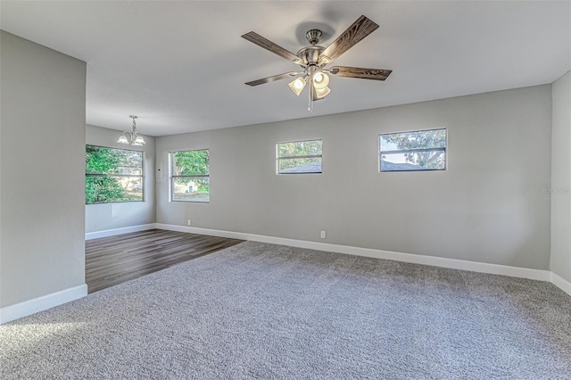 unfurnished room featuring baseboards, dark colored carpet, and ceiling fan with notable chandelier