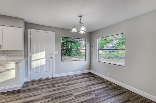 unfurnished dining area featuring a textured ceiling, baseboards, a chandelier, and wood finished floors