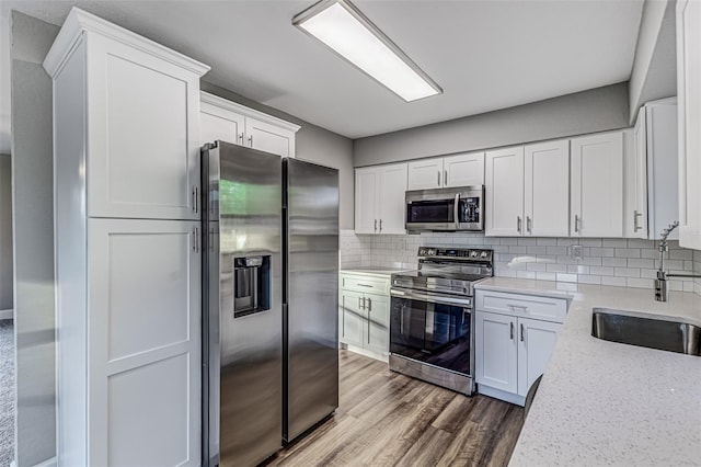 kitchen featuring stainless steel appliances, decorative backsplash, white cabinetry, a sink, and wood finished floors