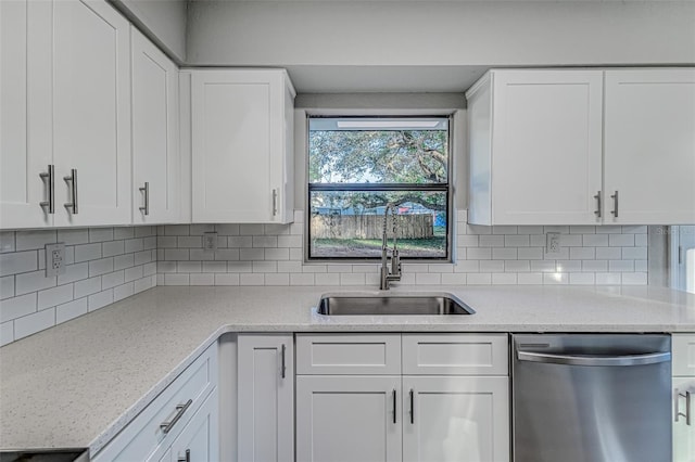 kitchen featuring tasteful backsplash, white cabinets, light stone counters, stainless steel dishwasher, and a sink