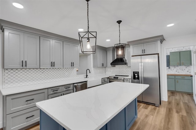 kitchen with wall chimney range hood, appliances with stainless steel finishes, pendant lighting, and gray cabinetry