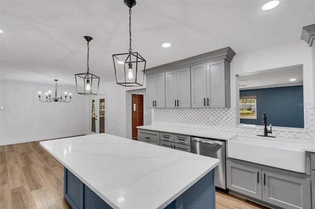 kitchen with tasteful backsplash, gray cabinets, stainless steel dishwasher, a kitchen island, and a sink