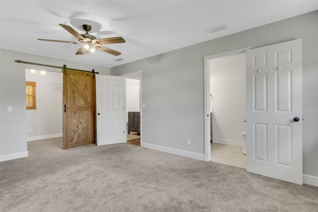 unfurnished bedroom featuring ensuite bath, a barn door, a spacious closet, and carpet flooring