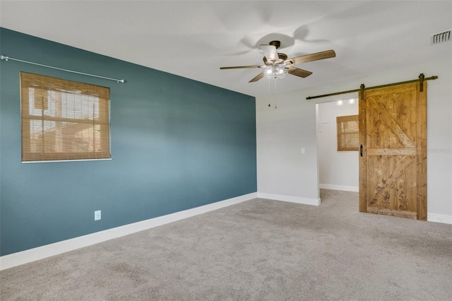 unfurnished room with carpet, visible vents, baseboards, and a barn door