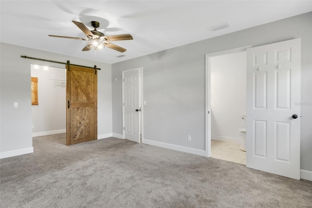 unfurnished bedroom featuring a closet, visible vents, a spacious closet, a barn door, and carpet flooring